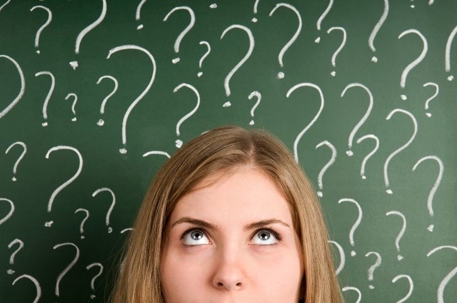 Woman standing in front of blackboard with question marks written all over